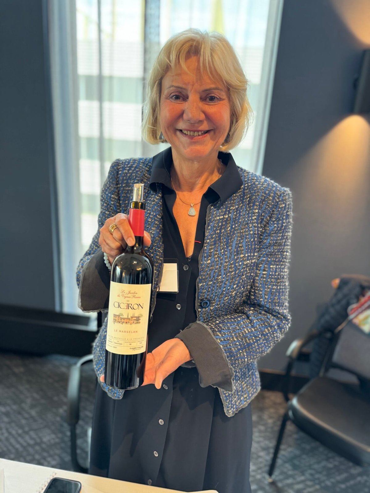 Lachende vrouw in blauw colbert houdt fles Domaine Cicéron Le Marselan rode wijn vast