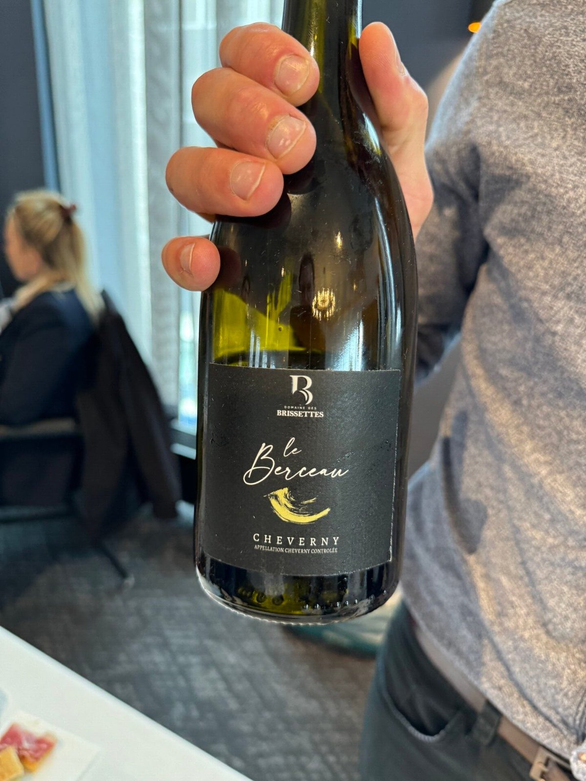 Hand houdt fles Domaine des Brissettes Le Berceau Cheverny met zwart etiket vast