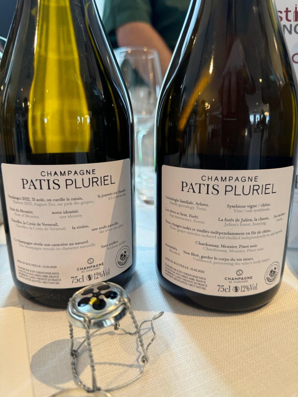 Achterkant van twee Patis Pluriel-flessen met Franse en Engelse tekst en muselet ervoor