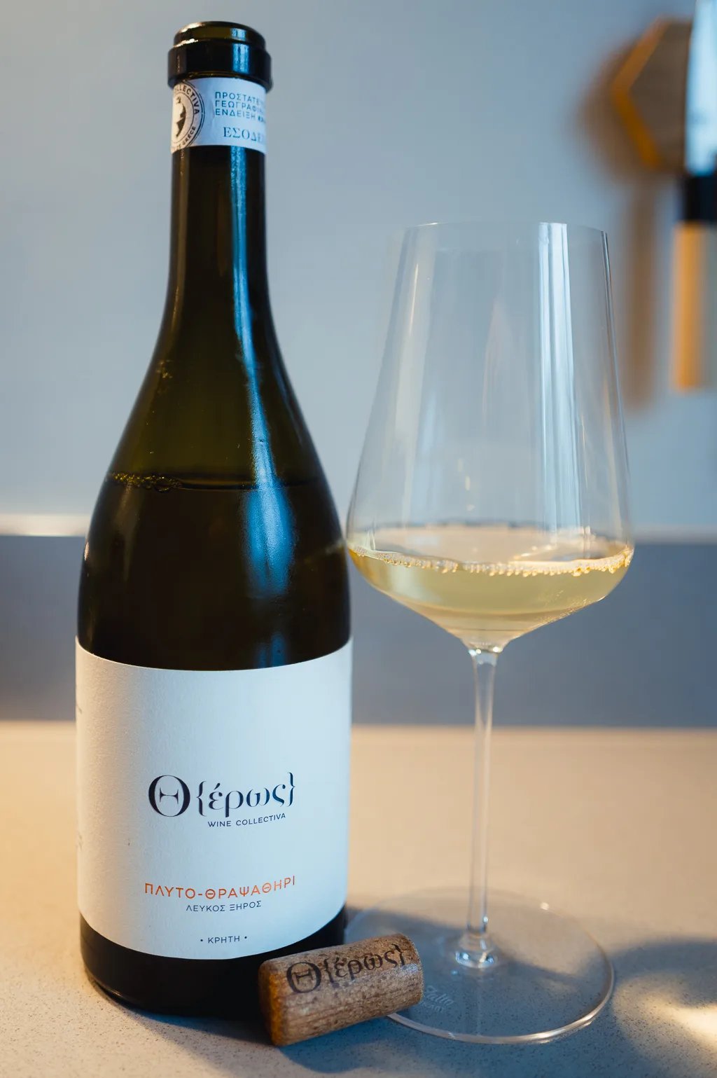 Fles Otheros Dafni-Vidiano witte wijn met glas lichtgele wijn en kurk op een aanrecht
