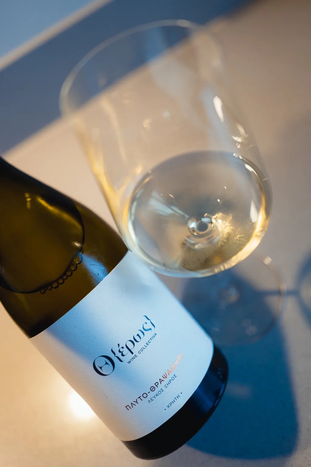 Fles Otheros Dafni-Vidiano van bovenaf naast een glas lichtgele Kretenzische wijn