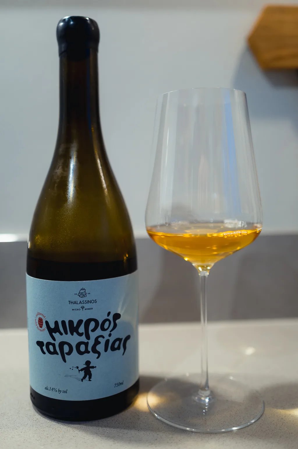 Fles Mikros Taraxias oranjewijn met blauw etiket naast glas amberkleurige wijn