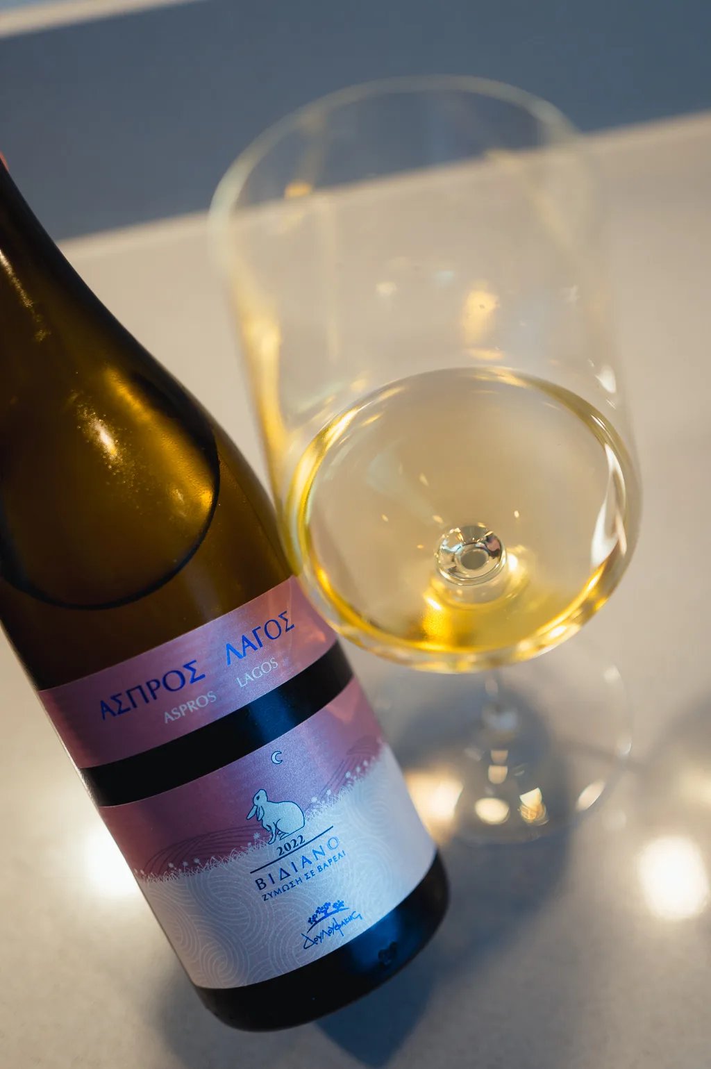 Fles Aspros Lagos Vidiano ligt naast een glas lichtgele wijn van bovenaf gezien