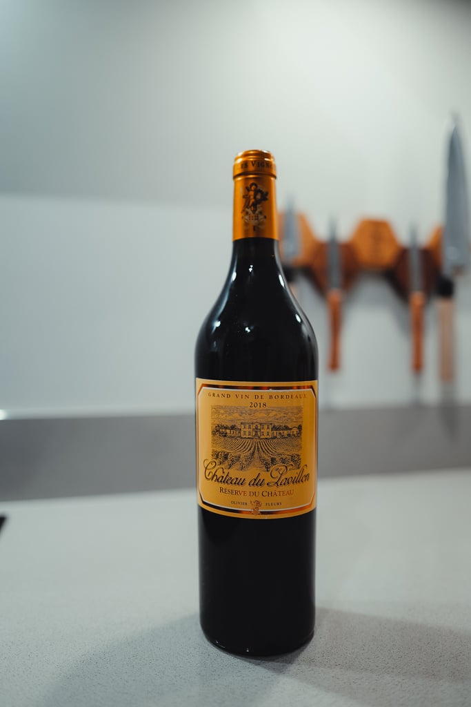 Hand houdt een fles Clos des Servitudes 2017 Cadillac vast naast een liggend glas rode wijn