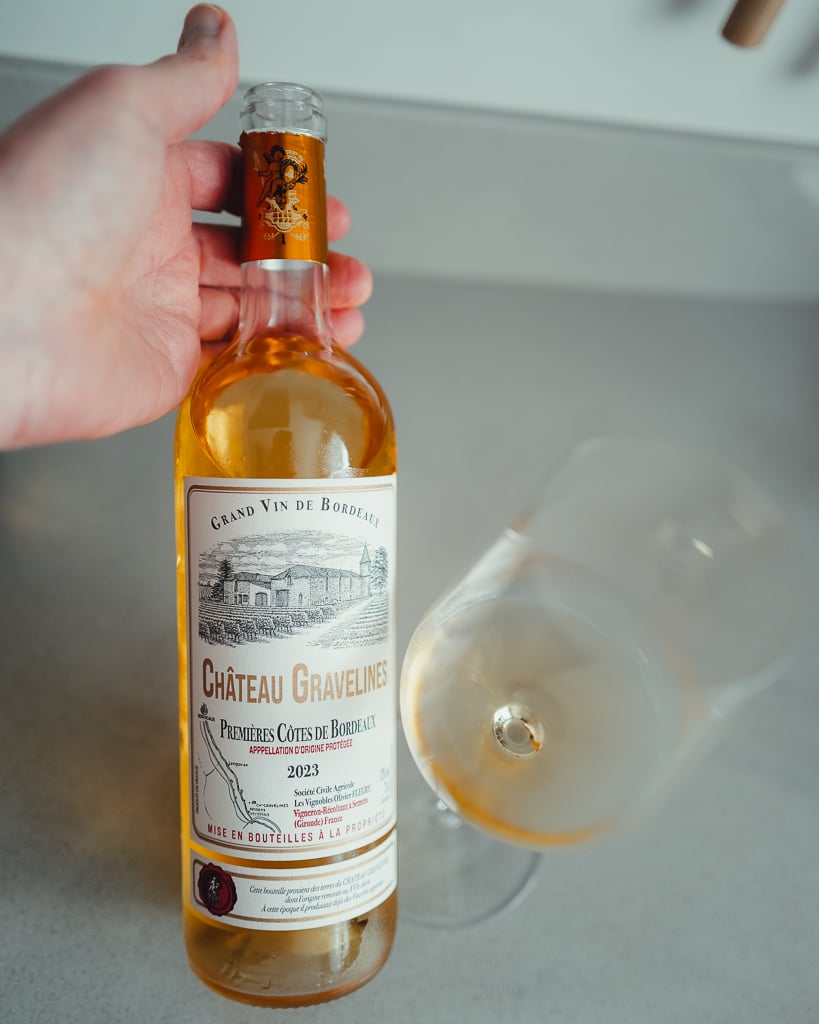 Hand houdt een fles Château Les Roques Loupiac 2017 vast met amberkleurige zoete wijn in de fles