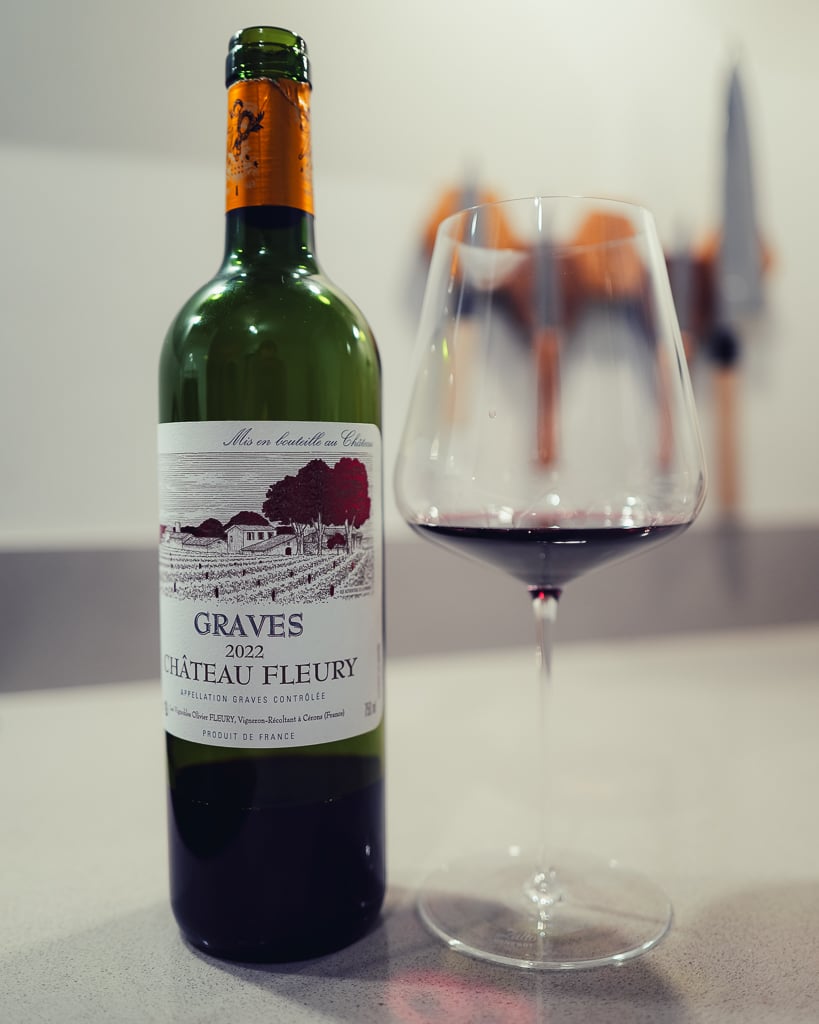 Fles Château Gravelines 2023 naast een glas amberkleurige zoete wijn op een aanrecht