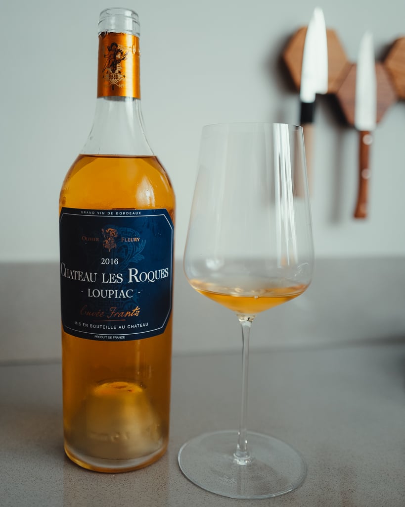 Fles Clos des Servitudes 2017 naast een glas rode wijn op een lichte aanrecht