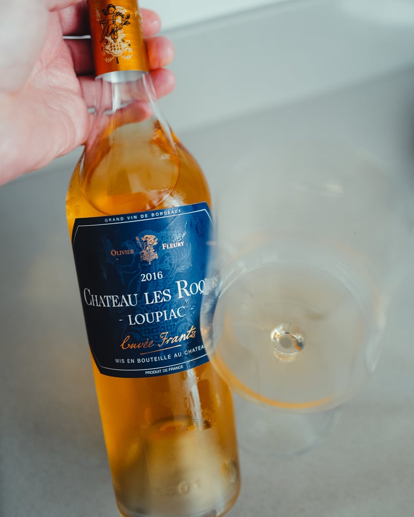 Fles Clos des Servitudes 2017 naast een glas rode wijn op een lichte aanrecht