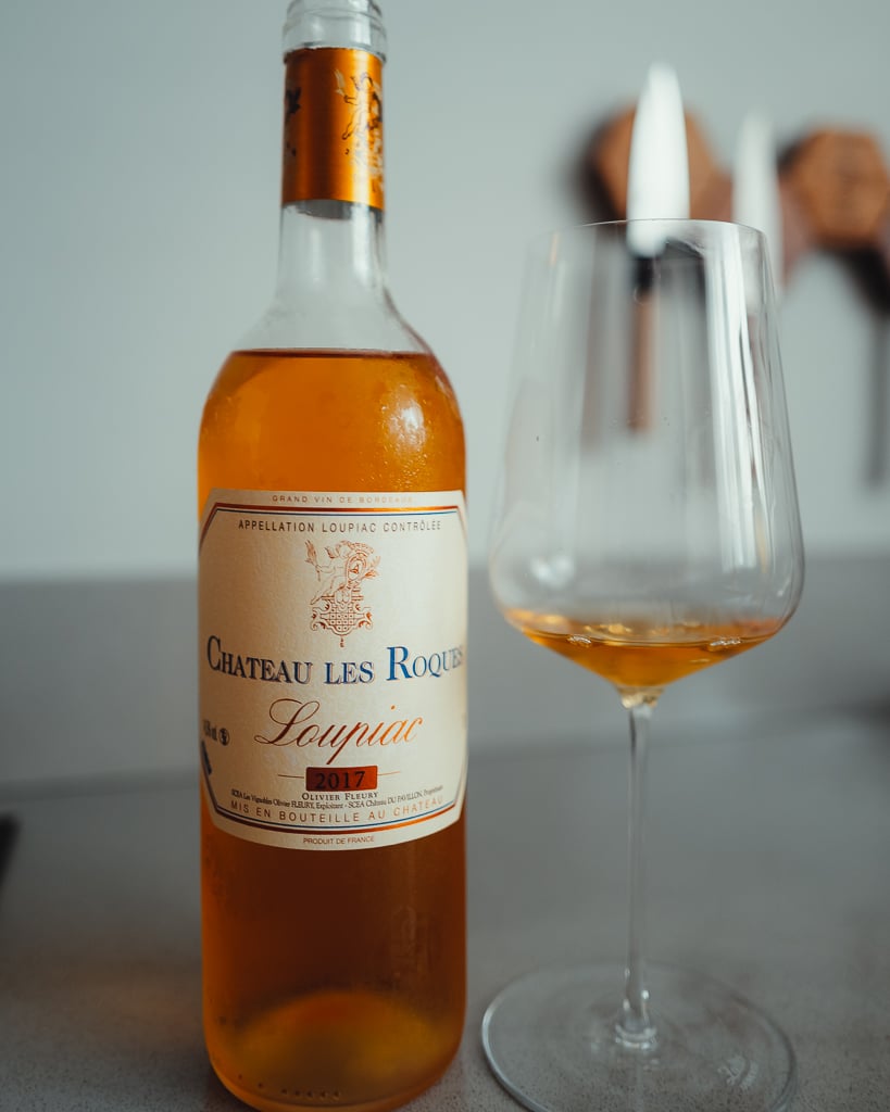 Fles Château Les Roques Loupiac 2017 naast een glas amberkleurige zoete wijn