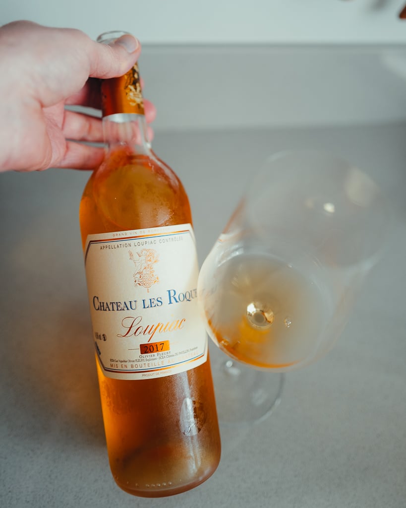 Fles Château Les Roques Loupiac 2016 met blauw etiket naast een glas amberkleurige wijn