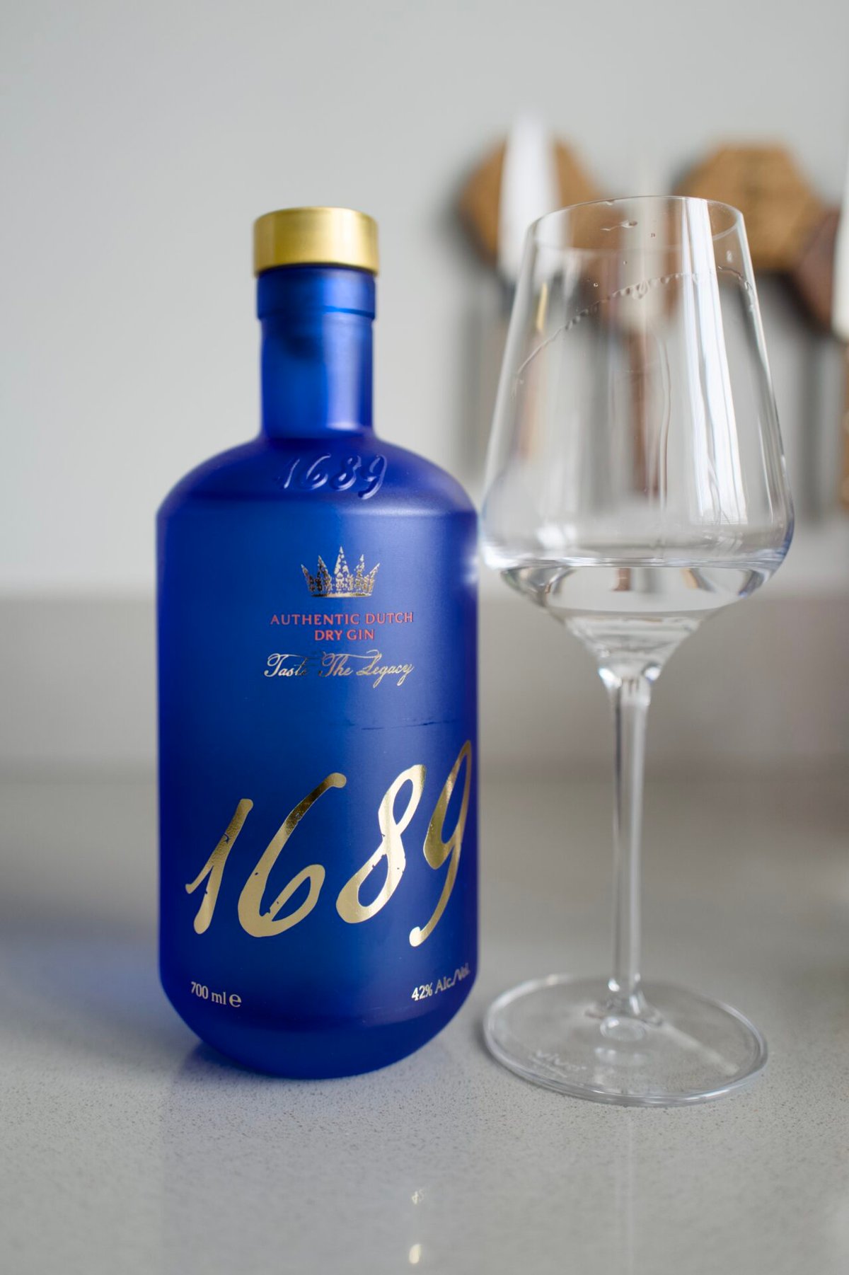 Blauwe fles 1689 Authentic Dutch Dry Gin met gouden dop naast een leeg wijnglas