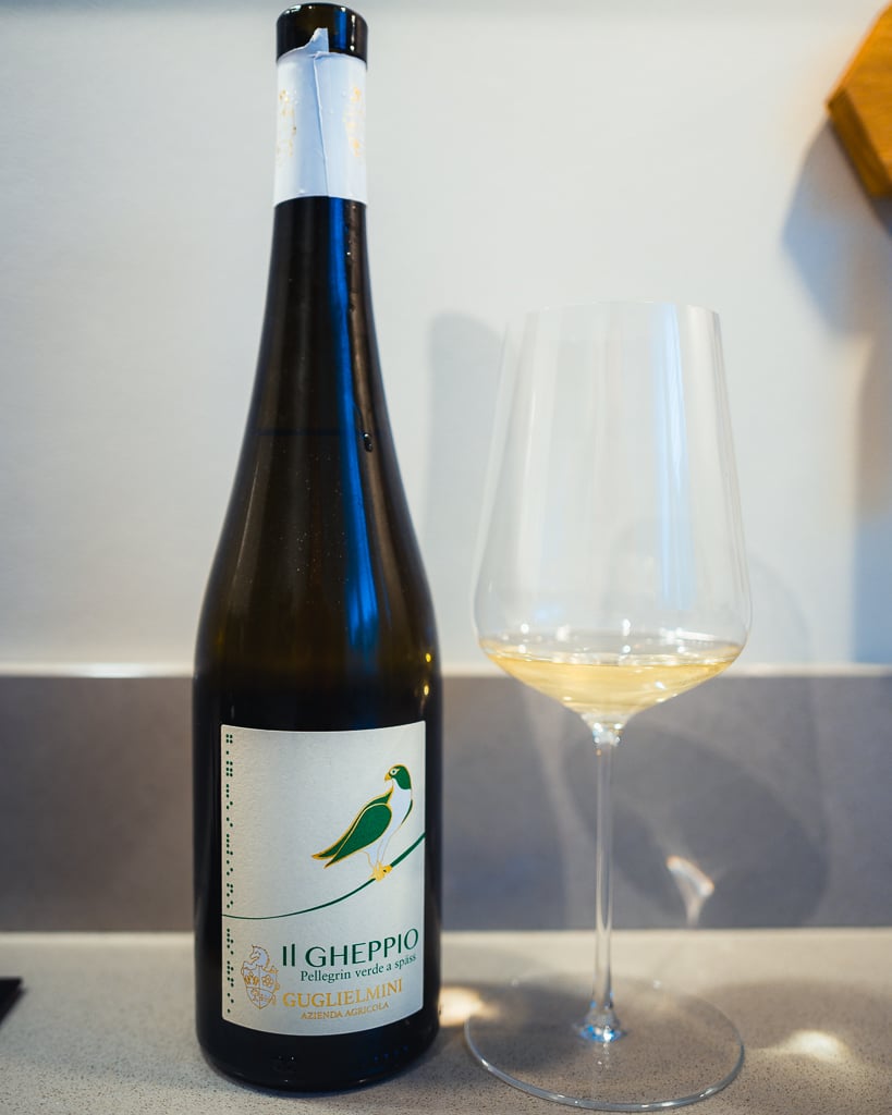 Fles Il Gheppio van Guglielmini met groene vogel op het etiket naast een glas witte wijn