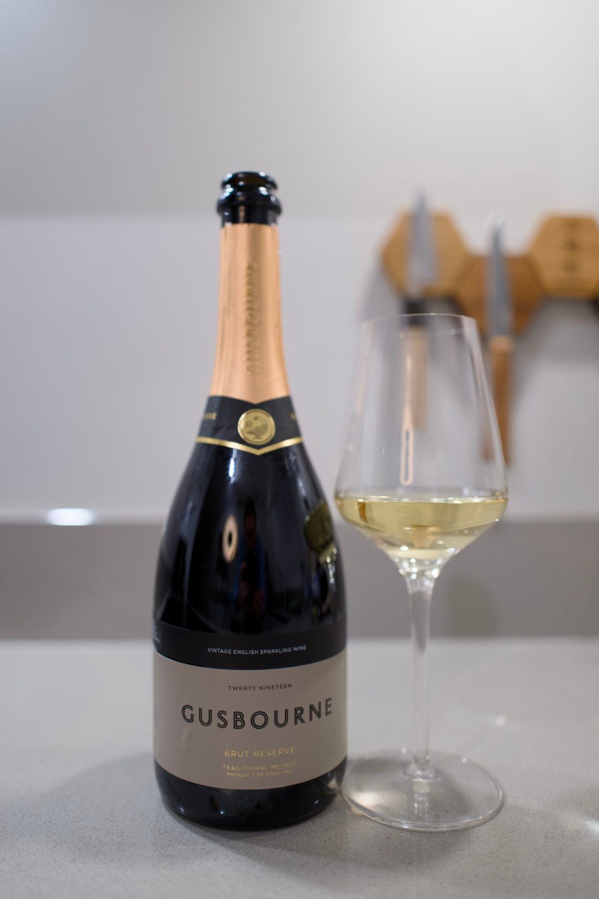 Fles Gusbourne Brut Reserve 2019 naast een glas witte wijn op een aanrecht