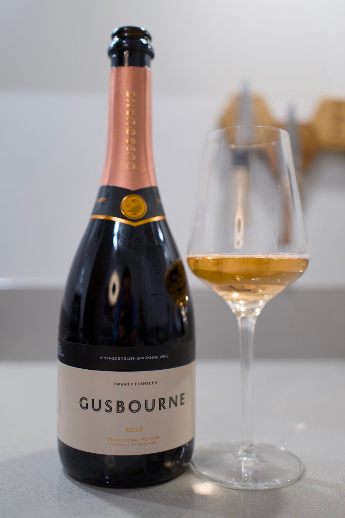 Fles Gusbourne Rosé 2018 naast een glas amberkleurige mousserende wijn