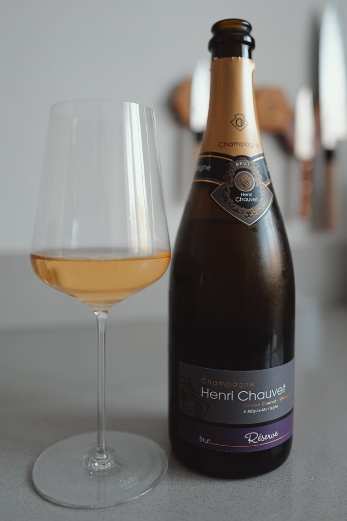 Glas amberkleurige champagne naast een fles Champagne Henri Chauvet Brut Réserve