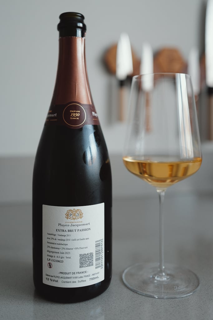 Achterkant van een fles Champagne Ployez-Jacquemart Extra Brut Passion naast een glas champagne