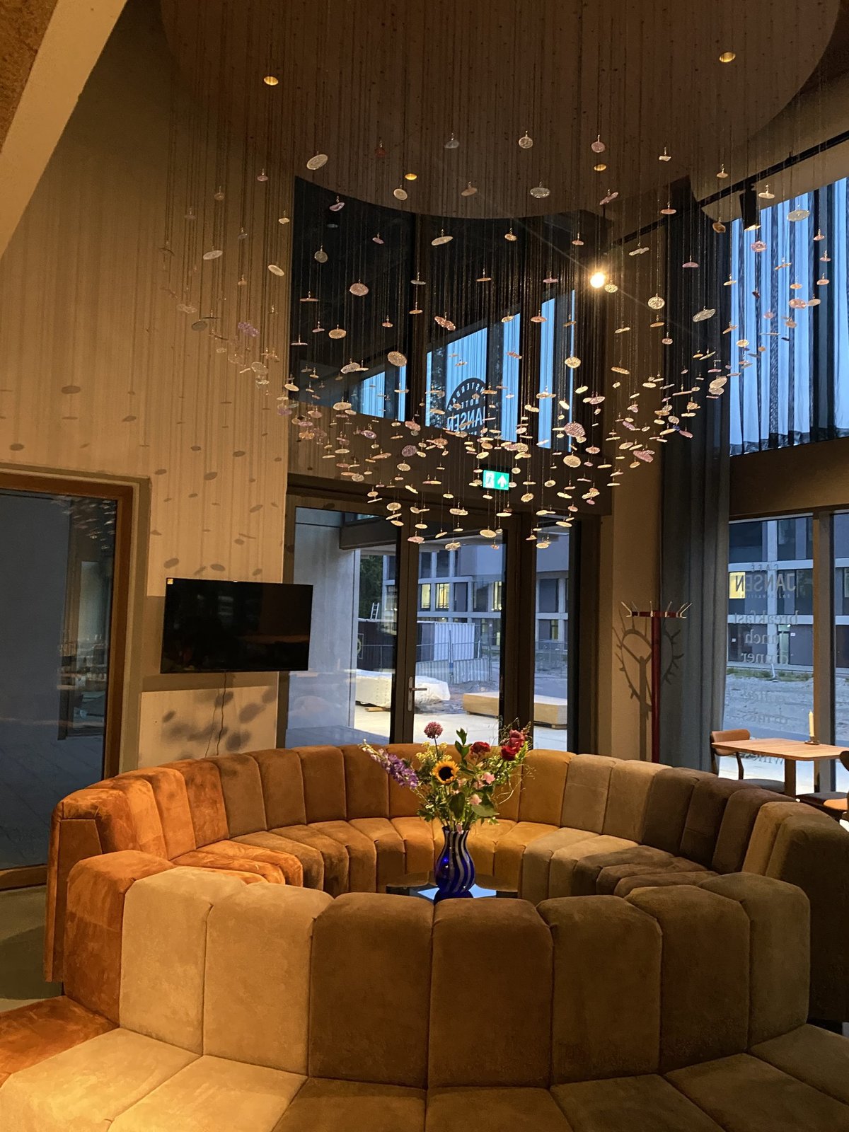 Hotellobby met grote ronde bank en hangende lichtinstallatie aan een hoog plafond
