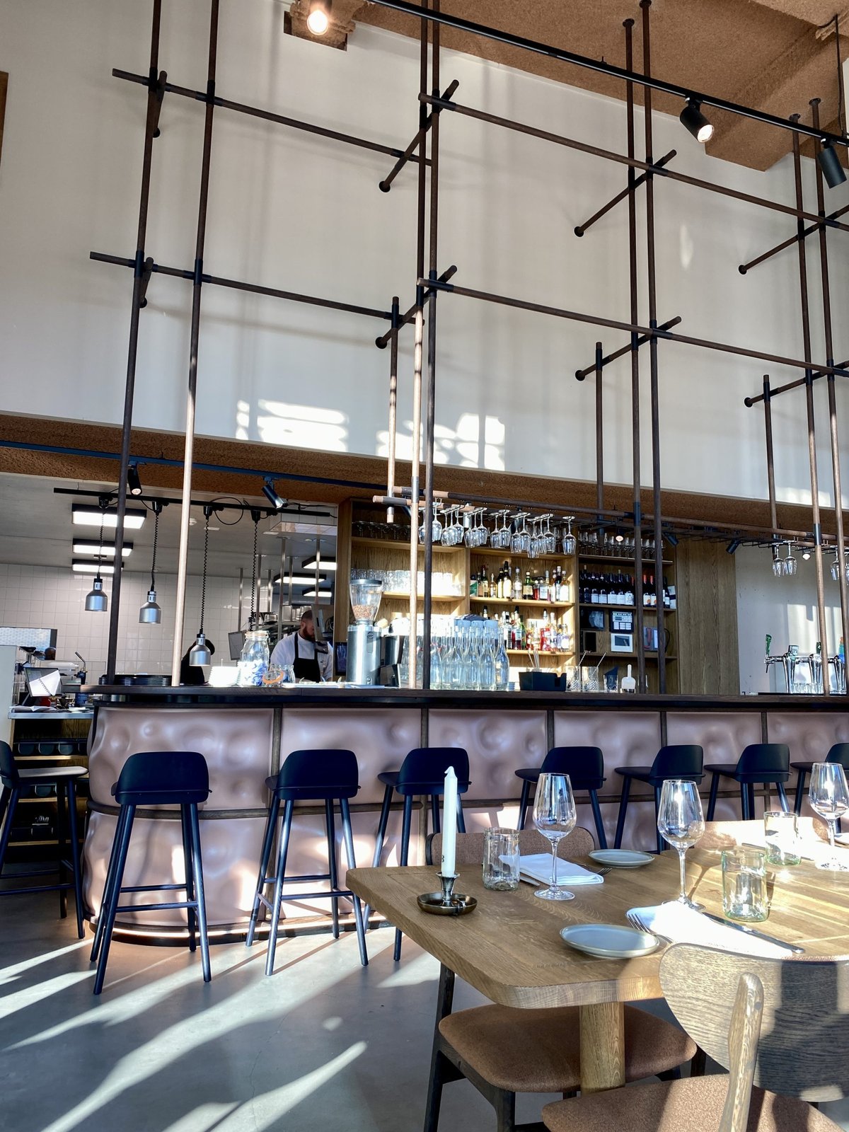 Interieur van restaurant met koperkleurige bar, blauwe krukken en hoog plafond