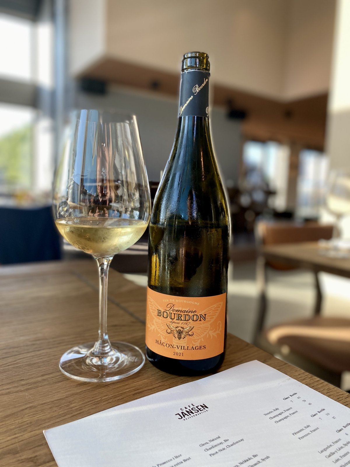 Glas witte wijn naast een fles Domaine Bourdon Mâcon-Villages op een restauranttafel