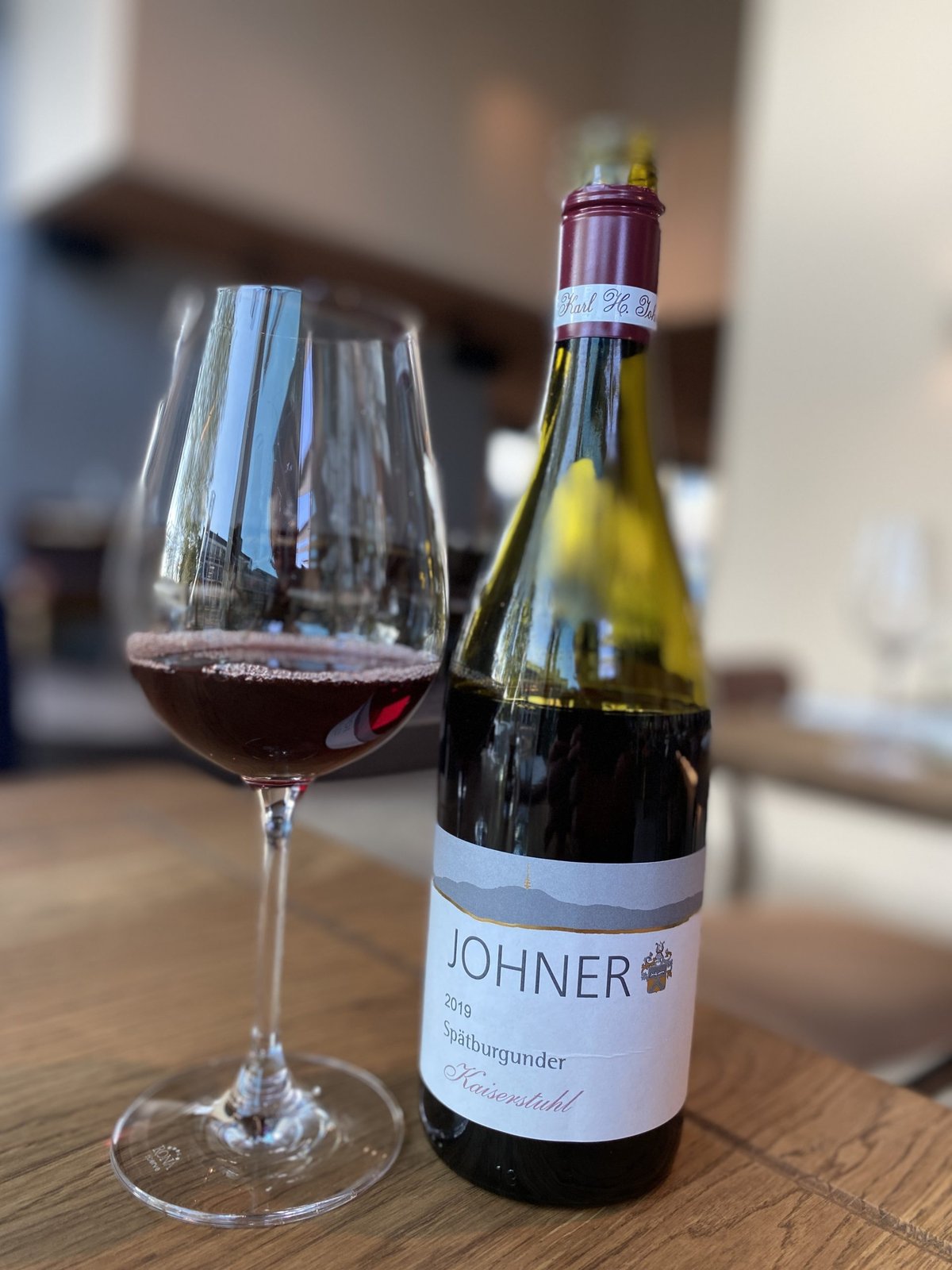 Glas rode wijn naast een fles Johner Spätburgunder Kaiserstuhl 2019 op een houten tafel