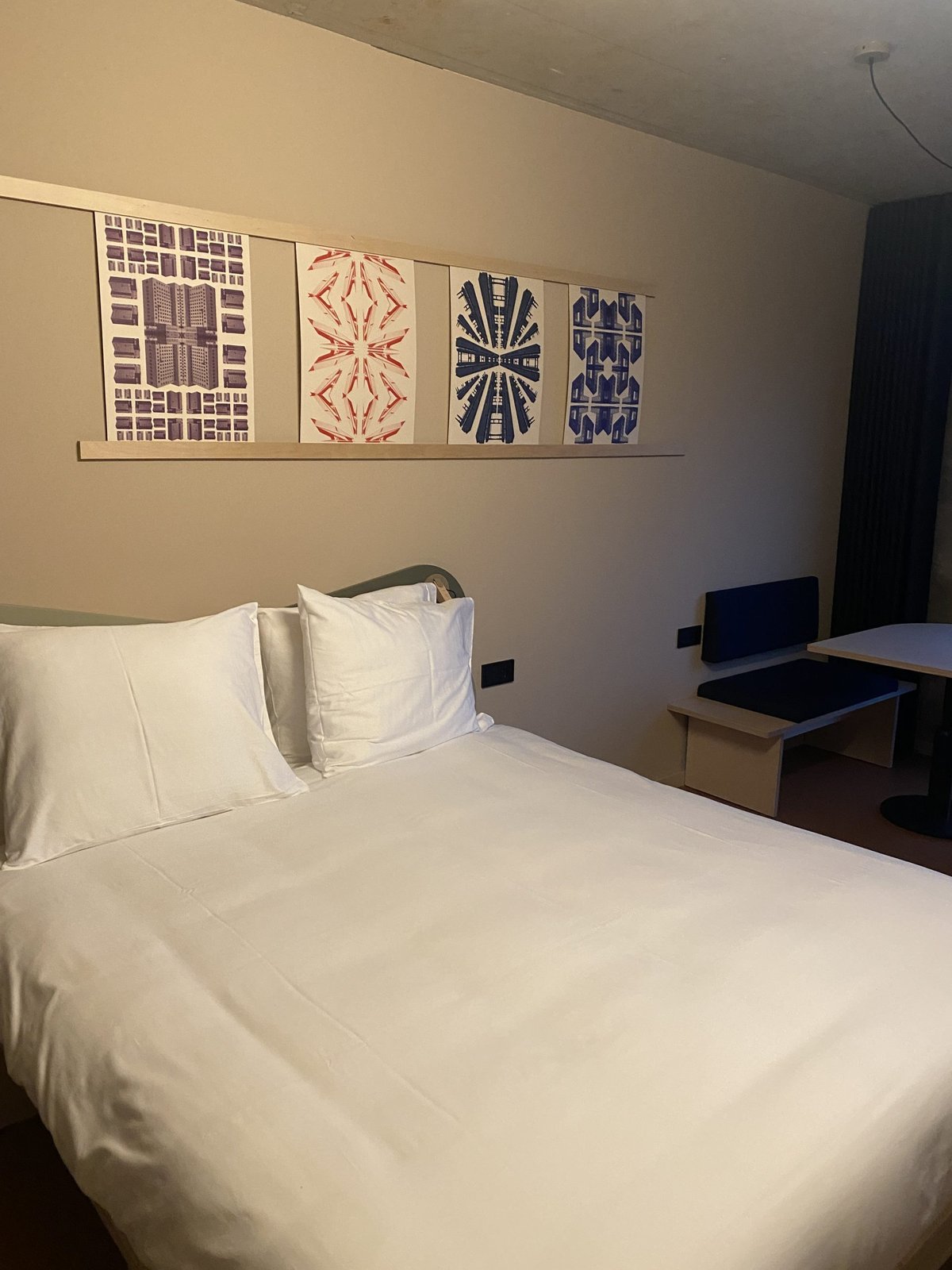 Hotelkamer met opgemaakt wit bed en vier grafische prenten boven het hoofdeinde