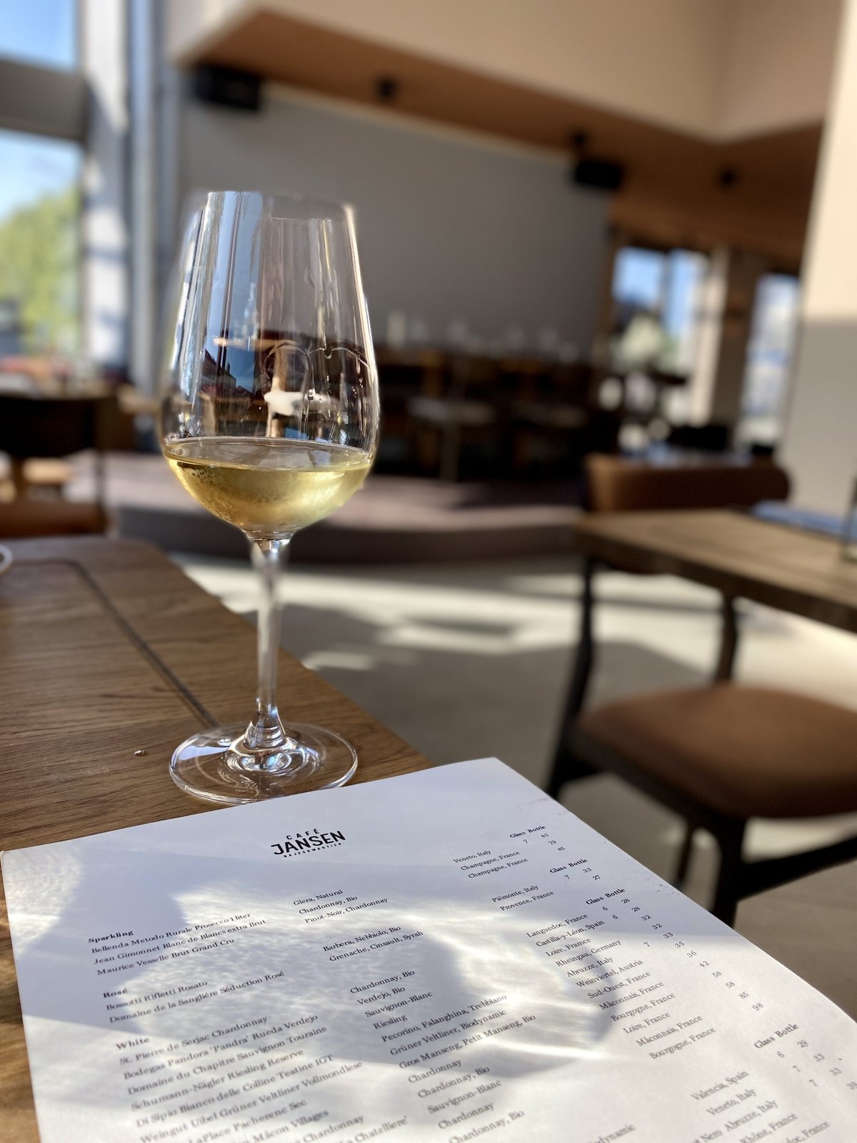 Glas witte wijn op een tafel met menukaart van Café Jansen in een licht restaurant