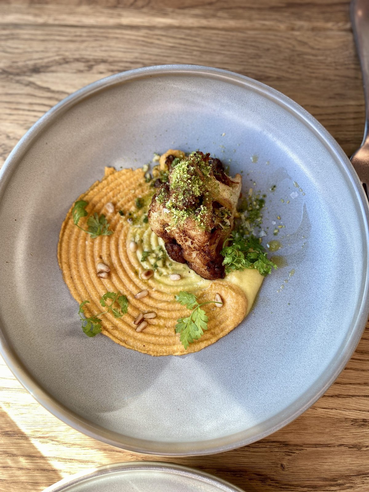 Bord met gebakken gerecht op een ronde puree met kruiden en pijnboompitten