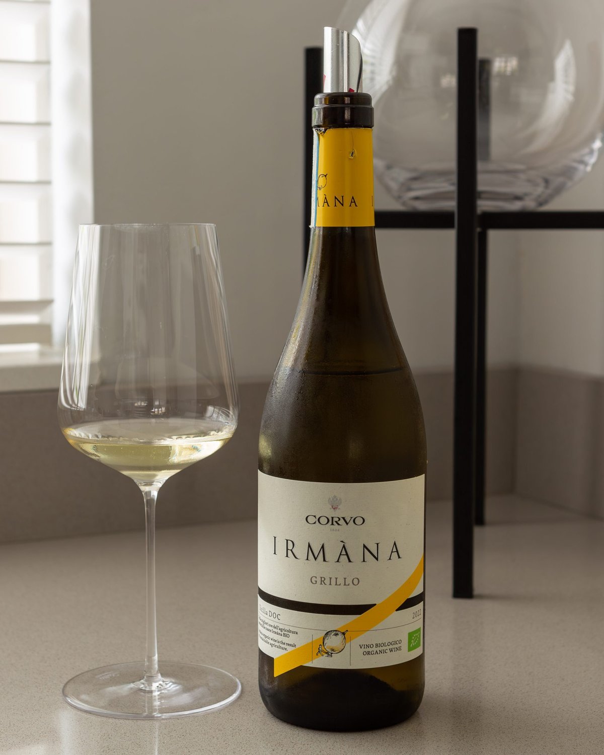 Glas witte wijn naast een fles Corvo Irmàna Grillo met gele accentband