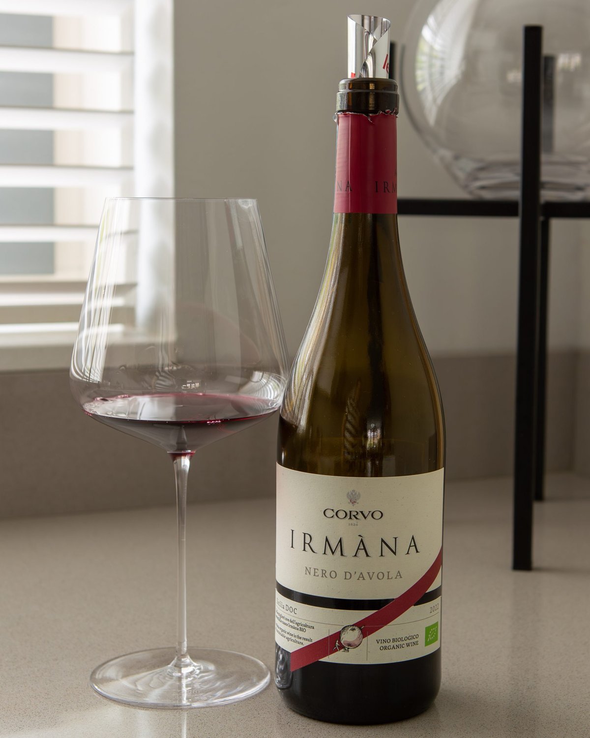 Glas rode wijn naast een fles Corvo Irmàna Nero d'Avola met rode schenktuit