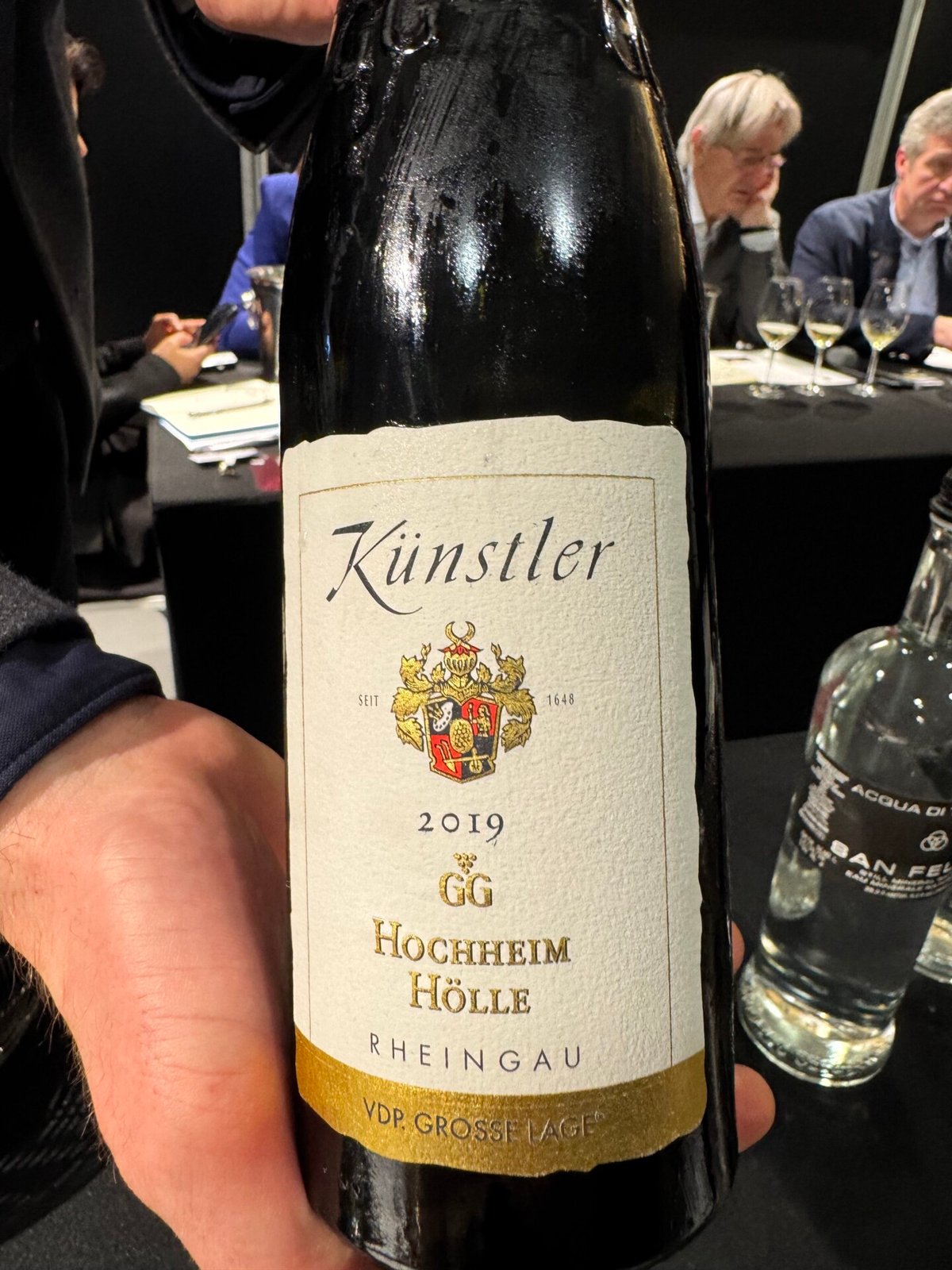 Hand holding a Kunstler 2019 GG Hochheim Holle Rheingau Riesling bottle at the tasting