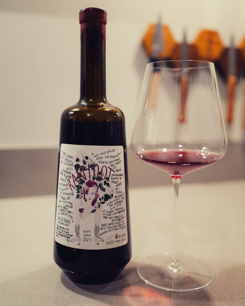 Fles Ranyoot Pinot Noir met kunstzinnig etiket naast een glas helderrode wijn op een aanrecht