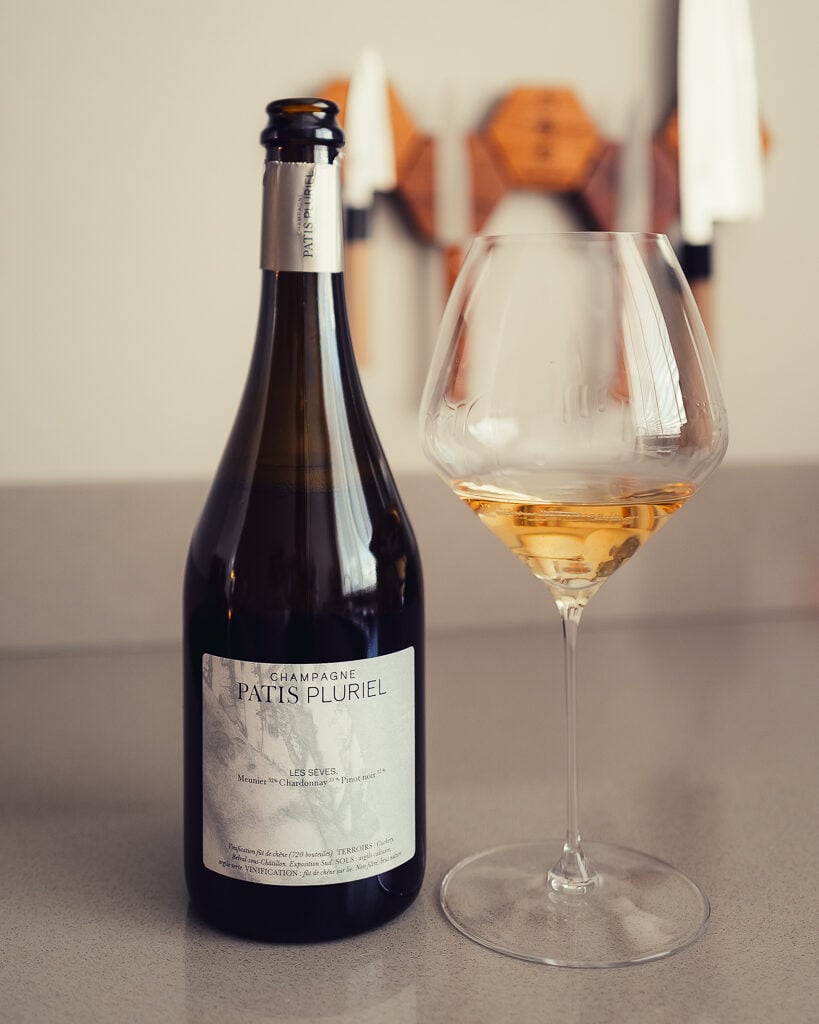 Fles Champagne Patis Pluriel Les Sèves naast een glas diepgele champagne op een aanrecht