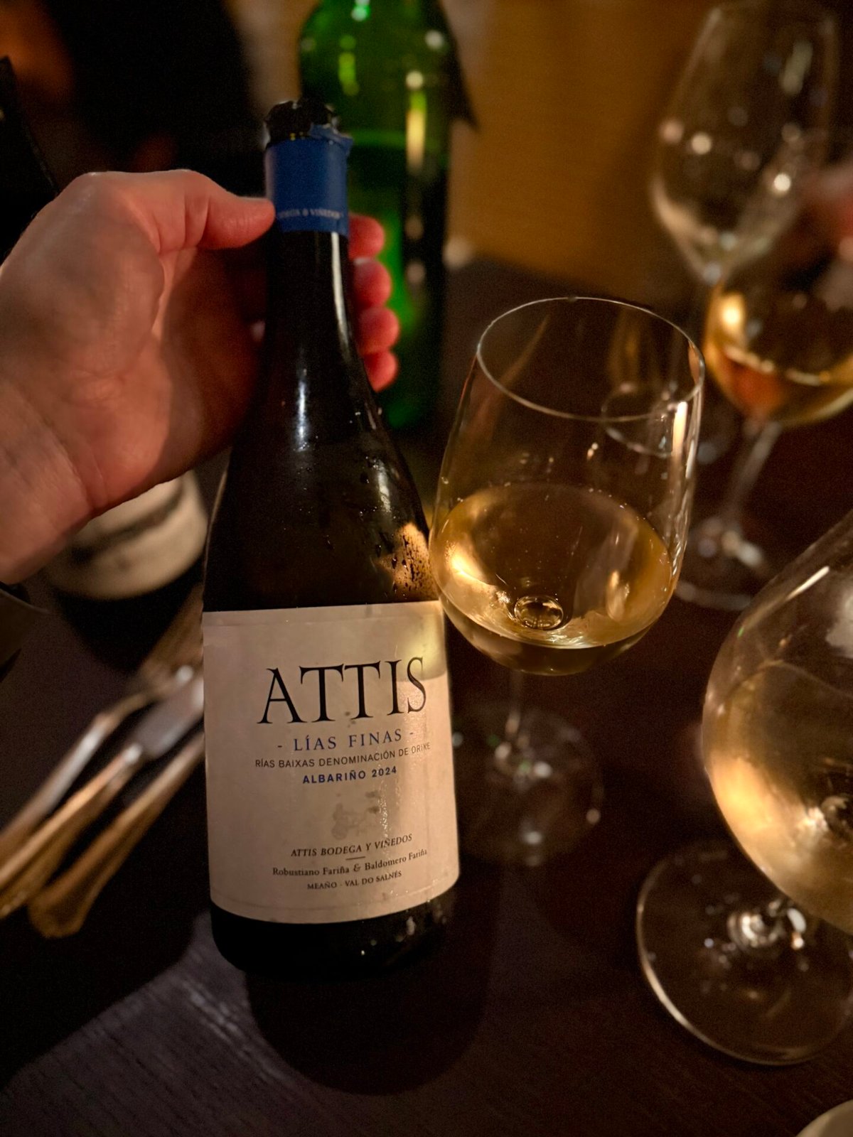 Hand houdt een fles Attis Lías Finas Albariño uit Rías Baixas vast naast een glas witte wijn