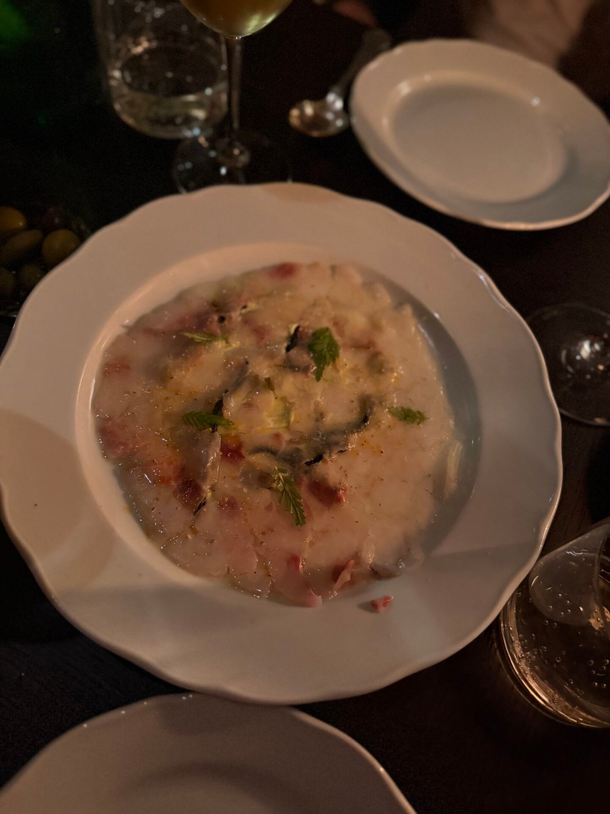 Witte diep bord met carpaccio van vis, muntblaadjes en stukjes garnituur in kaarslicht
