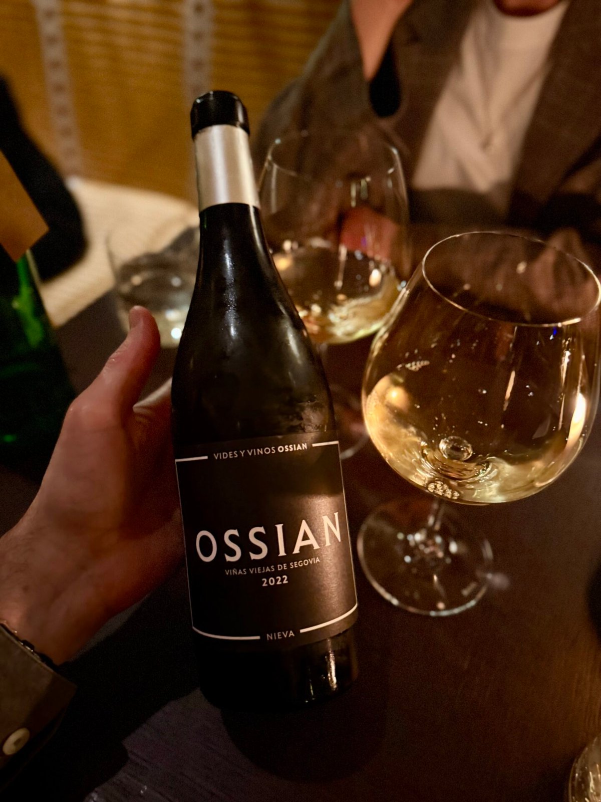 Hand houdt een fles Ossian Viñas Viejas Verdejo uit Segovia vast naast glazen witte wijn