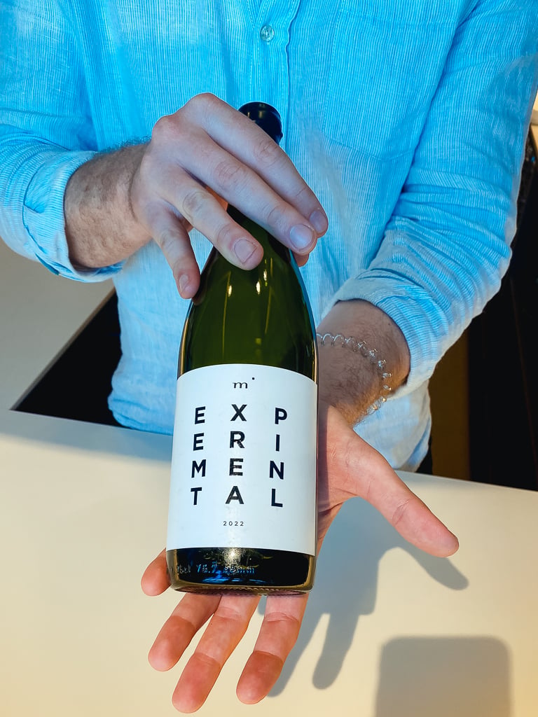 Hand presenteert op de palm een fles Minimalist EXPERIMENTAL met wit etiket in groen glas