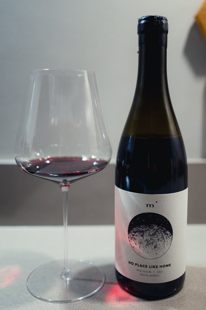 Fles Minimalist No Place Like Home Syrah naast een glas rode wijn op een aanrecht
