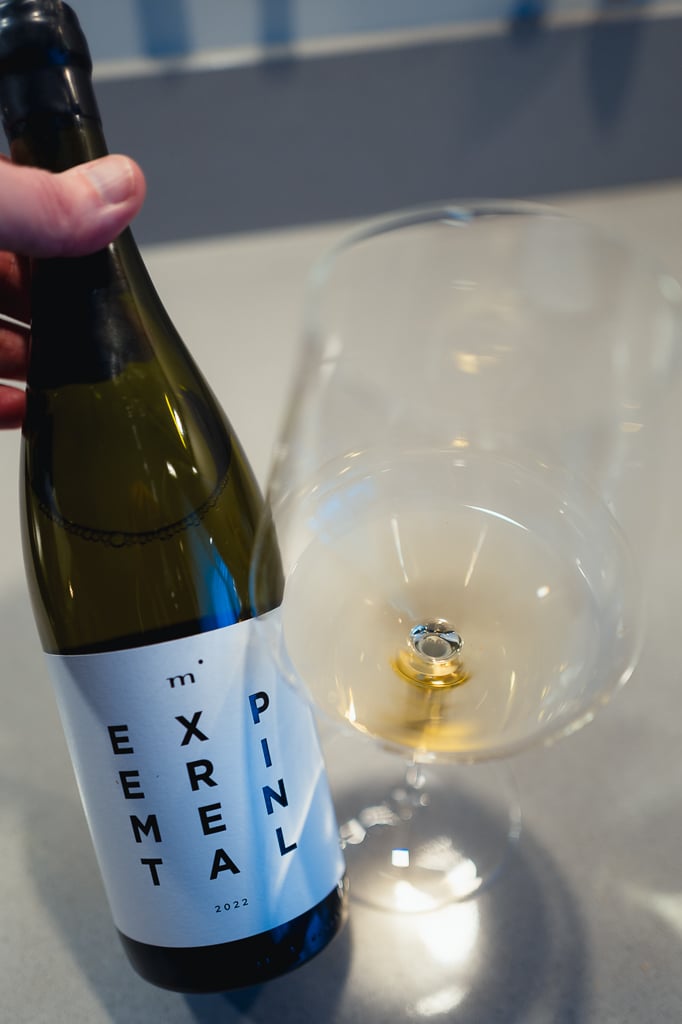Hand houdt de fles Minimalist EXPERIMENTAL met wit etiket vast naast een glas witte wijn