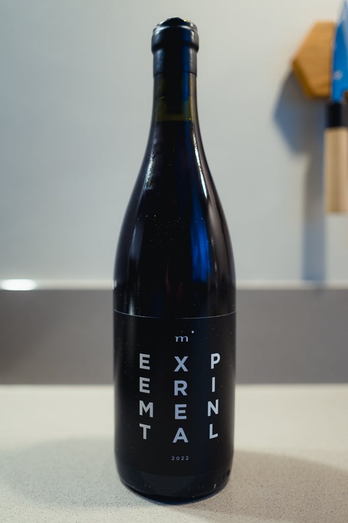 Donkere fles Minimalist EXPERIMENTAL met zwart etiket alleen op een aanrecht voor een grijze muur