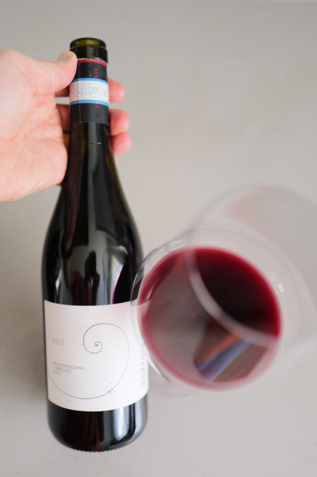 Hand houdt de fles La Valentina Montepulciano d'Abruzzo DOC vast naast een liggend glas rode wijn