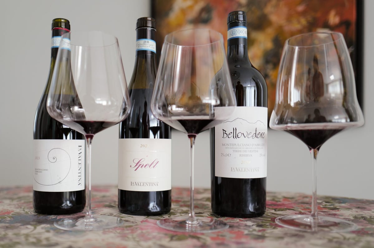 Drie flessen rode La Valentina Montepulciano naast wijnglazen met rode wijn op bloemenkleed