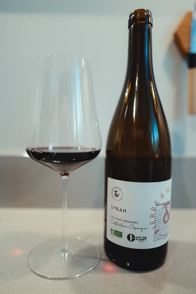 Fles Pierre & Nico Syrah biologisch met glas donkerrode wijn ervoor op aanrecht