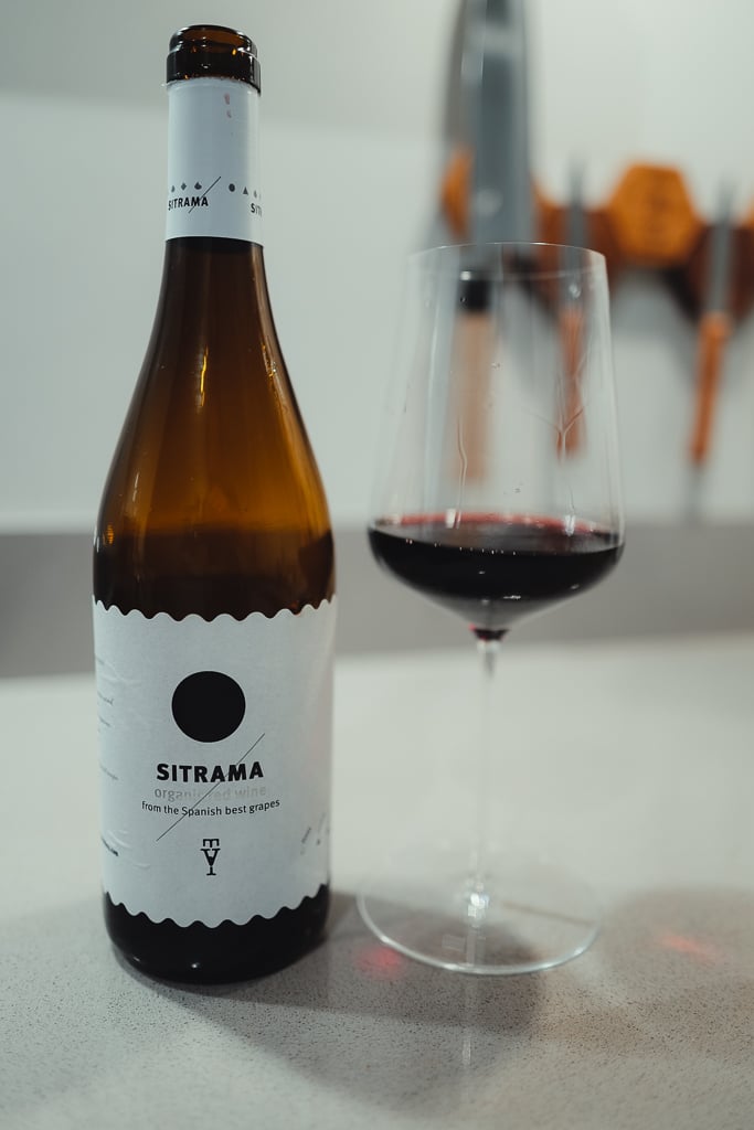Fles Sitrama organic red wine naast glas donkerrode wijn op aanrecht