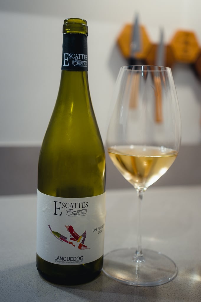 Groene fles Escattes Languedoc witte wijn naast glas met goudgele wijn op aanrecht