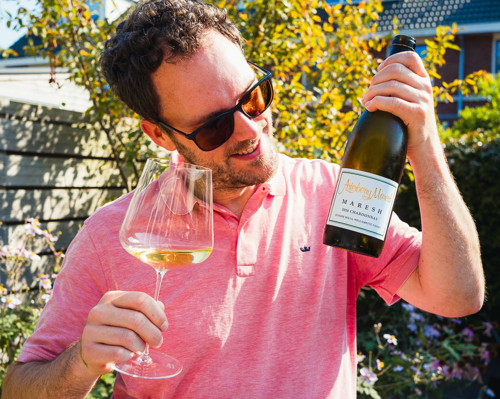 Man met zonnebril ruikt aan glas witte wijn terwijl hij fles Arterberry Maresh vasthoudt in tuin