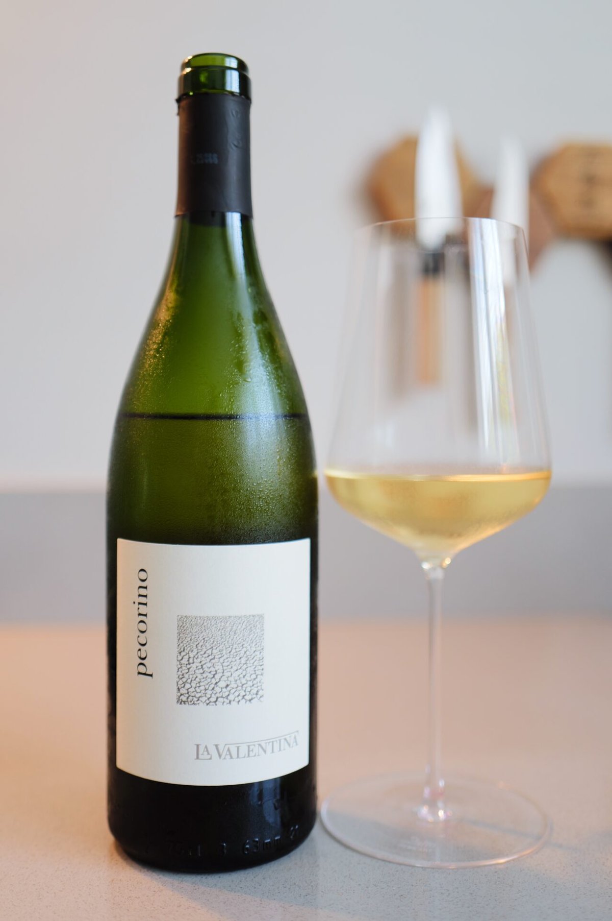 Fles La Valentina Pecorino naast glas lichtgele witte wijn op aanrecht