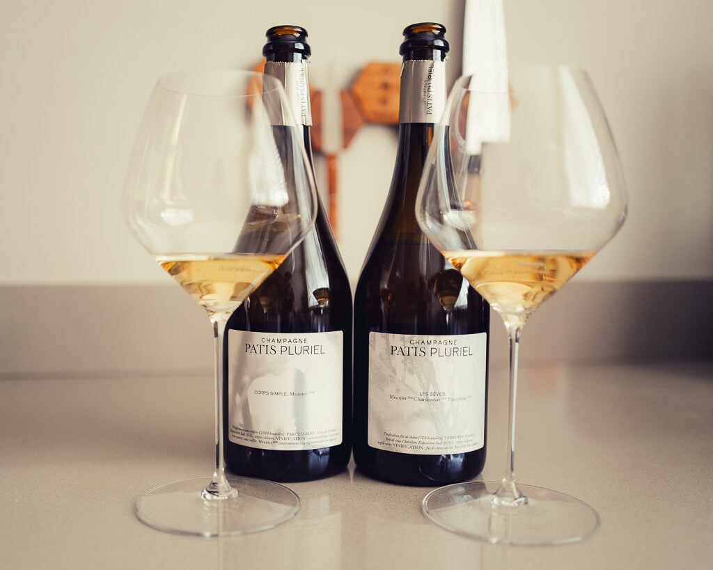 Twee flessen Champagne Patis Pluriel met champagneglazen ertussen op aanrecht