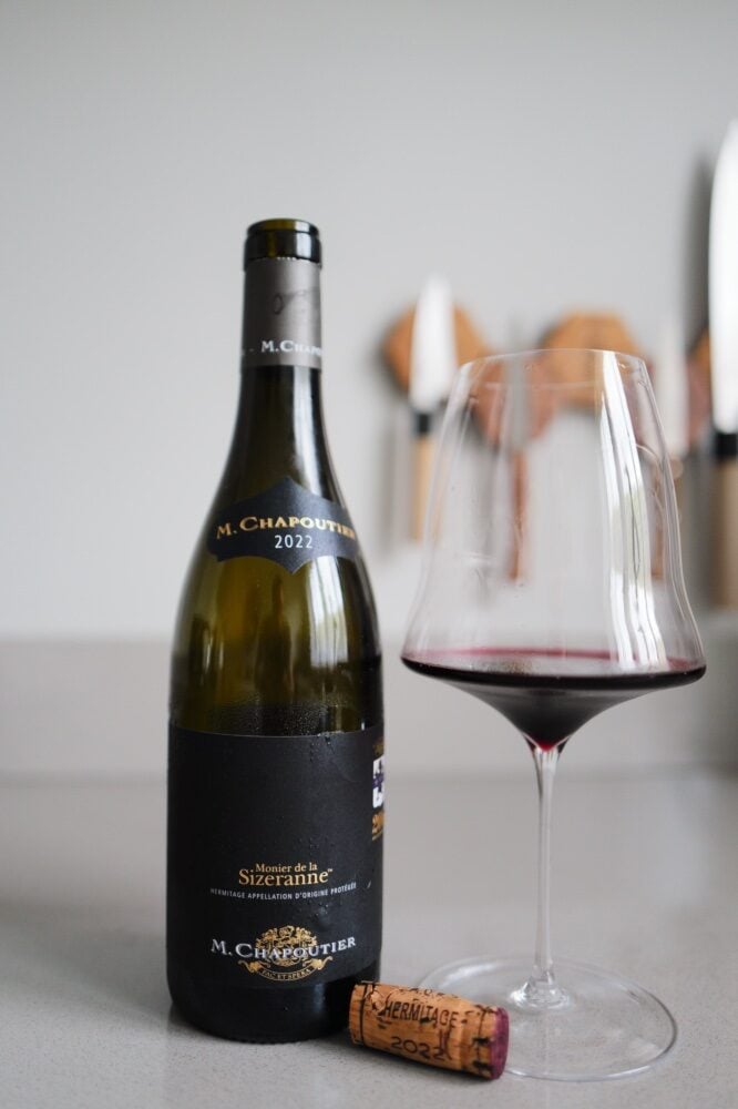 Fles M. Chapoutier Monier de la Sizeranne Hermitage naast glas rode wijn met kurk