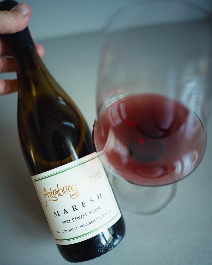 Hand houdt fles Arterberry Maresh Pinot Noir schuin naast liggend glas lichtrode wijn
