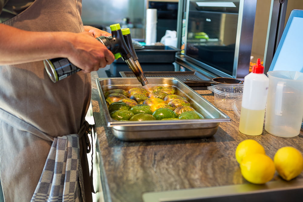 Kok brandt met gasbrander courgettes op een plaat in een open keuken